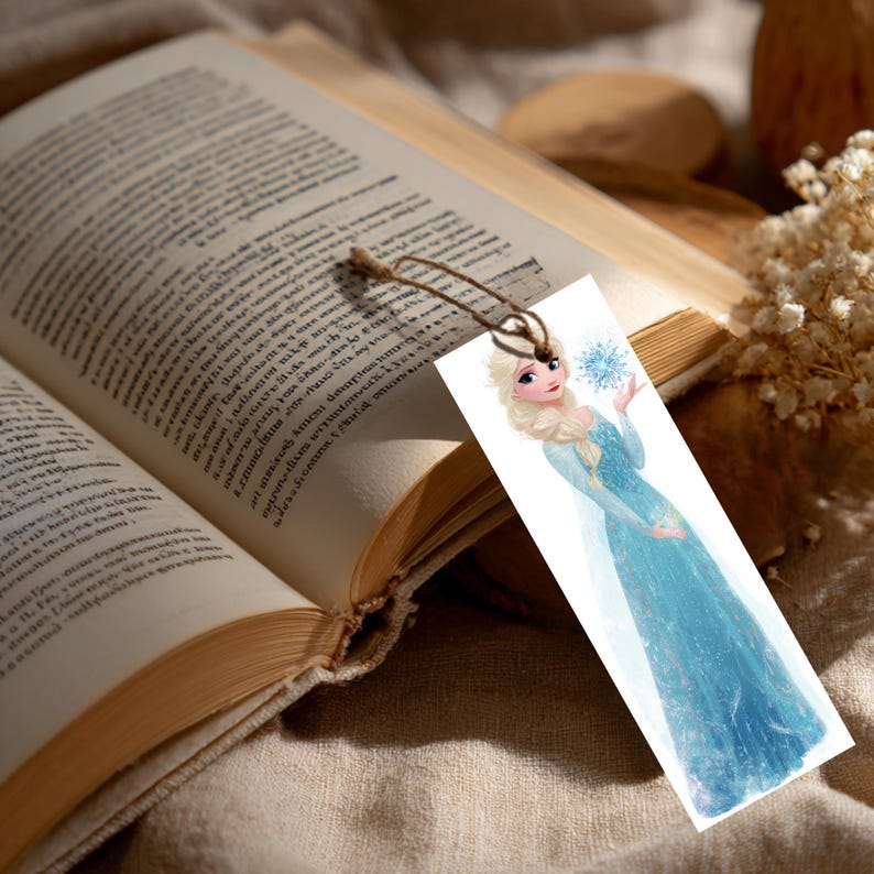 Peut inclure: Un marque-page rectangulaire en papier blanc orn&eacute; d'une illustration imprim&eacute;e d'un personnage blond aux cheveux tress&eacute;s portant une longue robe bleu clair scintillante, tenant un flocon de neige bleu, avec une fine boucle en ficelle brune.