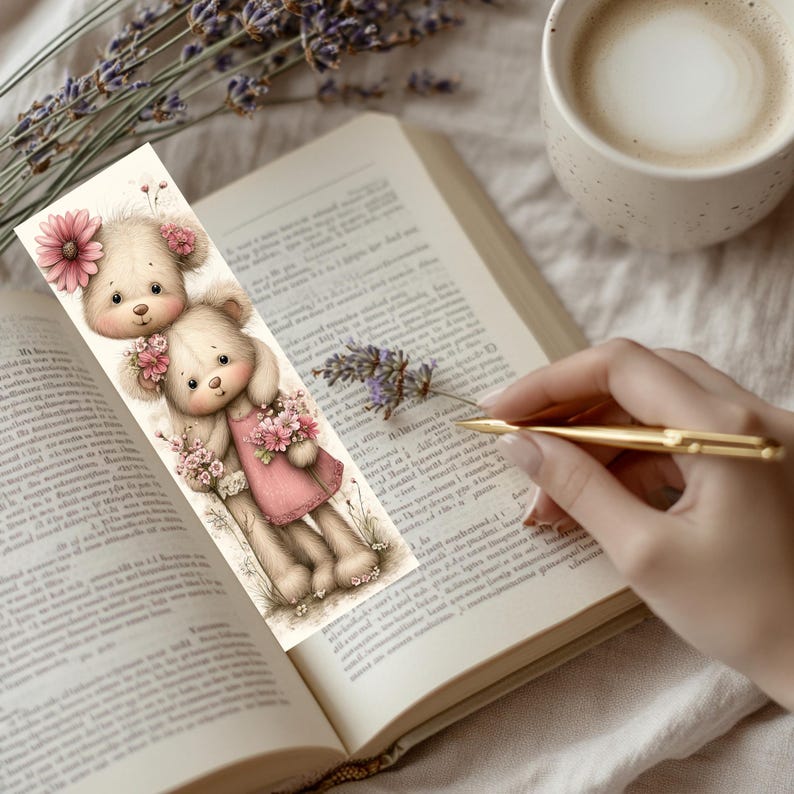 May include: A whimsical bookmark featuring two teddy bears with pink flower accents. One bear wears a pink dress and holds a bouquet. The bookmark is placed in an open book, with a cup of coffee and lavender sprigs nearby.