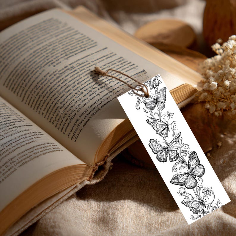 Op de afbeelding: Een rechthoekige boekenlegger van wit papier met een gedetailleerde zwarte inktillustratie van meerdere vlinders en krullende bloemranken. De boekenlegger heeft een klein gaatje aan de bovenkant met een dun bruin touwtje eraan.