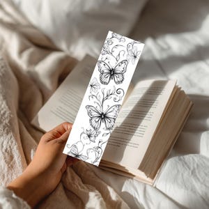 Op de afbeelding: Een rechthoekige boekenlegger met een zwart-witte lijntekening van vlinders en krullende bloemenranken. Het ontwerp is gedrukt op een witte achtergrond en toont gedetailleerde vleugels en verfijnde botanische elementen in de verticale lay-out.