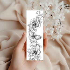 Op de afbeelding: Een rechthoekige boekenlegger met een zwart-witte lijntekening van drie vlinders omringd door diverse florale elementen en krullende rankpatronen, gerangschikt in een verticale compositie op een witte achtergrond.