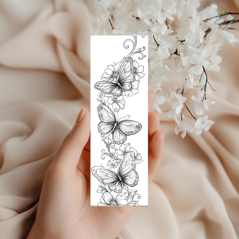 Op de afbeelding: Een rechthoekige boekenlegger met een zwart-witte lijntekening van drie vlinders omringd door diverse florale elementen en krullende rankpatronen, gerangschikt in een verticale compositie op een witte achtergrond.