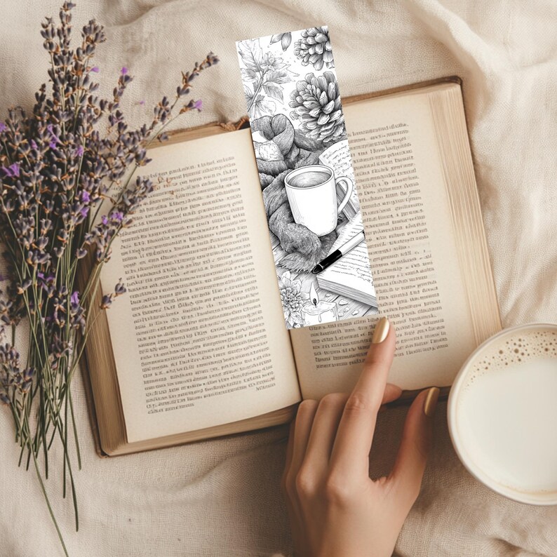 May include: A black and white bookmark featuring a cozy scene with a coffee mug, scarf, and pen, set against a backdrop of leaves and pinecones. The bookmark is placed in an open book, with a sprig of lavender and a cup of coffee in the scene.