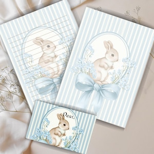 May include: Stationery set featuring a light blue and white striped pattern. Each piece has a watercolor illustration of a bunny surrounded by blue flowers and a light blue bow. The set includes a lined notebook, a blank notebook, and a card that says "Dear,"