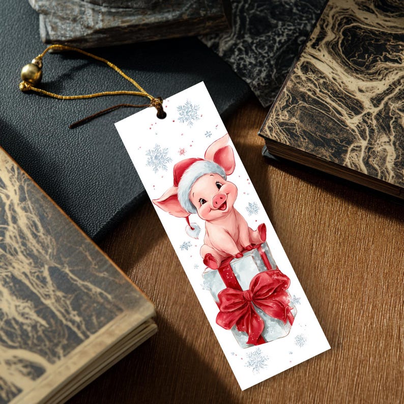 Peut inclure: Un marque-page rectangulaire blanc illustr&eacute; d'un porcelet rose portant un bonnet de P&egrave;re No&euml;l rouge et blanc, assis sur un cadeau orn&eacute; d'un grand n&oelig;ud rouge. Le motif inclut des flocons bleu clair et un cordon dor&eacute; avec une perle dor&eacute;e.