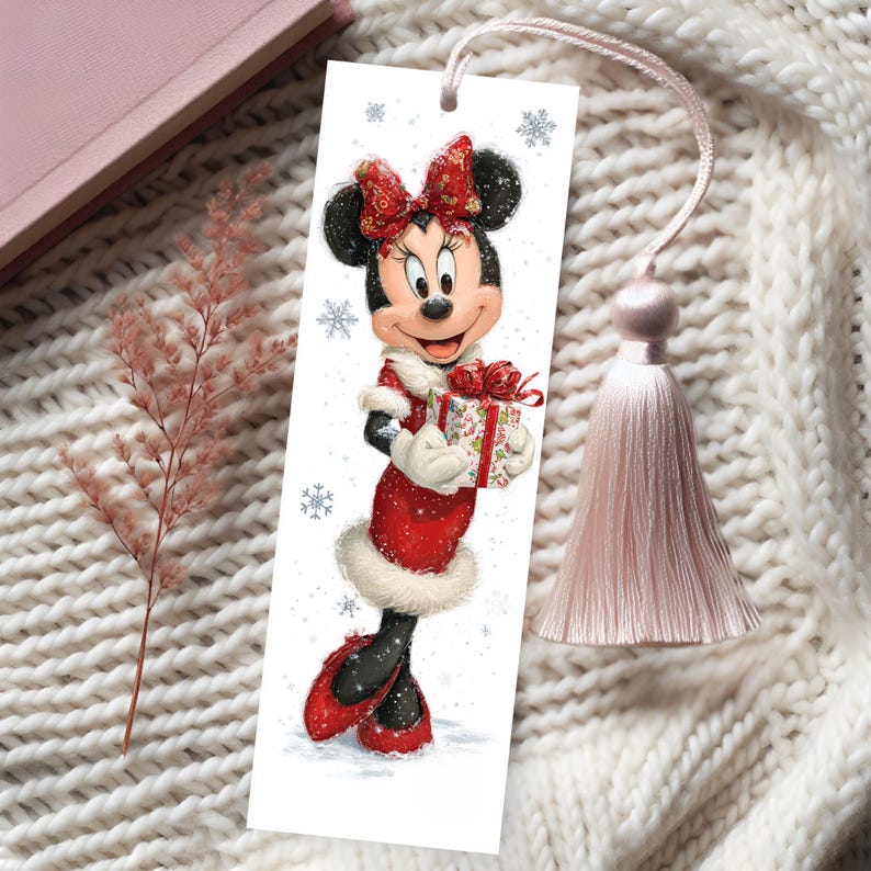 Peut inclure: Un marque-page rectangulaire en papier illustr&eacute; d'une souris de dessin anim&eacute; portant une robe rouge &agrave; bordure en fourrure blanche, un n&oelig;ud rouge assorti et tenant un cadeau. Le motif inclut des flocons bleus et un pompon rose p&acirc;le au sommet.