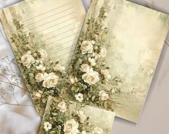 Könnte beinhalten: Briefpapier-Set im Vintage-Stil mit floralem Design. Das Set enthält liniertes und unliniertes Papier sowie eine kleine Karte. Cremefarbene Rosen und grüne Blätter zieren die Ränder des Papiers, vor einem weichen, gedämpften Hintergrund.