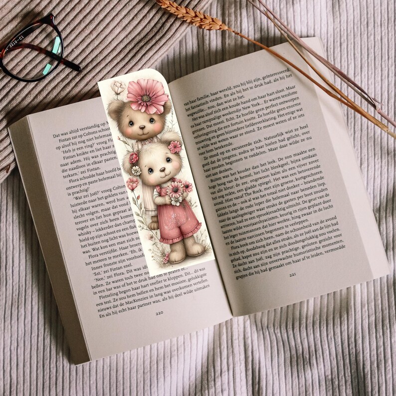 May include: A whimsical bookmark featuring two teddy bears with floral accents. The bears are in a soft, pastel color palette, holding flowers, and set against a delicate, illustrated background. The bookmark is placed in an open book.