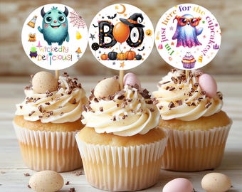 Peut inclure: Trois cupcakes avec glaçage blanc, copeaux de chocolat et décorations de Halloween. Les décorations présentent un monstre, le mot « BOO » et un fantôme. Des œufs décoratifs sont dispersés autour des cupcakes.