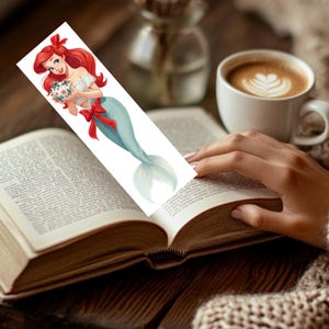 Peut inclure: Un marque-page rectangulaire pr&eacute;sentant une illustration de dessin anim&eacute; d'une sir&egrave;ne aux longs cheveux roux, portant un haut blanc &agrave; &eacute;paules d&eacute;nud&eacute;es et une queue bleu clair. La sir&egrave;ne tient un petit ornement floral blanc et un grand n&oelig;ud rouge.