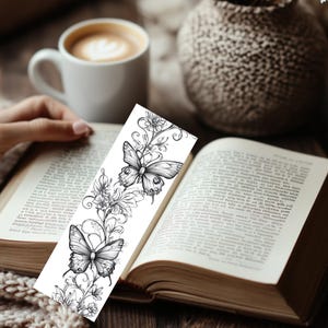 Op de afbeelding: Een rechthoekige boekenlegger met een gedetailleerde zwart-wit lijntekening van twee vlinders omringd door ingewikkelde bloemenranken en bladeren. Het ontwerp is gedrukt op een witte achtergrond met duidelijke, scherpe inktlijnen.