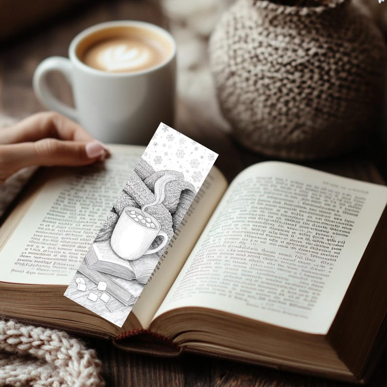 May include: A black and white bookmark featuring a cozy illustration of a mug of hot cocoa, a knitted scarf, and books. The bookmark is placed in an open book, with a cup of coffee in the background. The theme is reading and comfort.