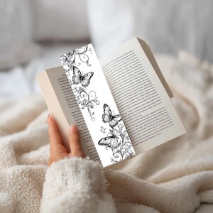 Op de afbeelding: Een rechthoekige boekenlegger met een zwart-witte lijntekening van drie vlinders omringd door ingewikkelde bloemen- en rankpatronen. Het ontwerp is gedrukt op een witte achtergrond en toont gedetailleerde vleugels en zwierige botanische elementen.