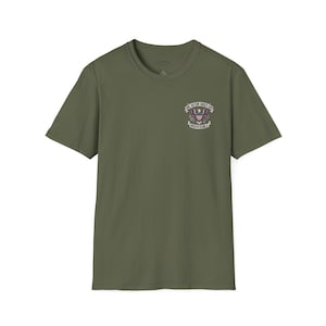 May include: An olive green short-sleeve t-shirt featuring a small graphic on the left chest. The graphic depicts a bald eagle with an American flag shield, surrounded by a banner with the text ONE NATION UNDER GOD INDIVISIBLE.