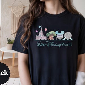 May include: Black t-shirt with a graphic of Walt Disney World icons, such as a castle, tree, and park logos. The words "Walt Disney World" are printed in teal below the graphic. The word "Black" is printed on a black circle.