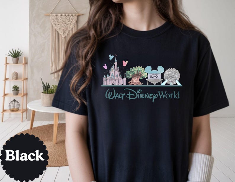 May include: Black t-shirt with a graphic of Walt Disney World icons, such as a castle, tree, and park logos. The words "Walt Disney World" are printed in teal below the graphic. The word "Black" is printed on a black circle.