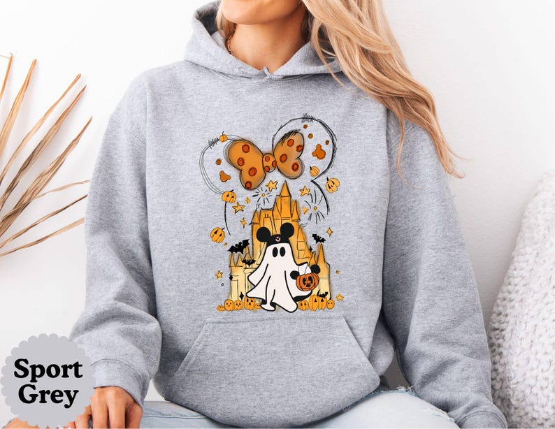 May include: A sport grey hooded sweatshirt featuring a graphic print of a ghost wearing mouse ears, standing in front of a castle. The design includes an orange polka-dot bow, small pumpkins, bats, and stars. The text Sport Grey is visible in a circle.