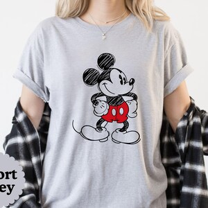 May include: Sport Grey t-shirt featuring a black and white sketch of Mickey Mouse with red shorts and white gloves and shoes. The shirt has rolled-up sleeves. The words "Sport Grey" are in a gray circle at the bottom left.