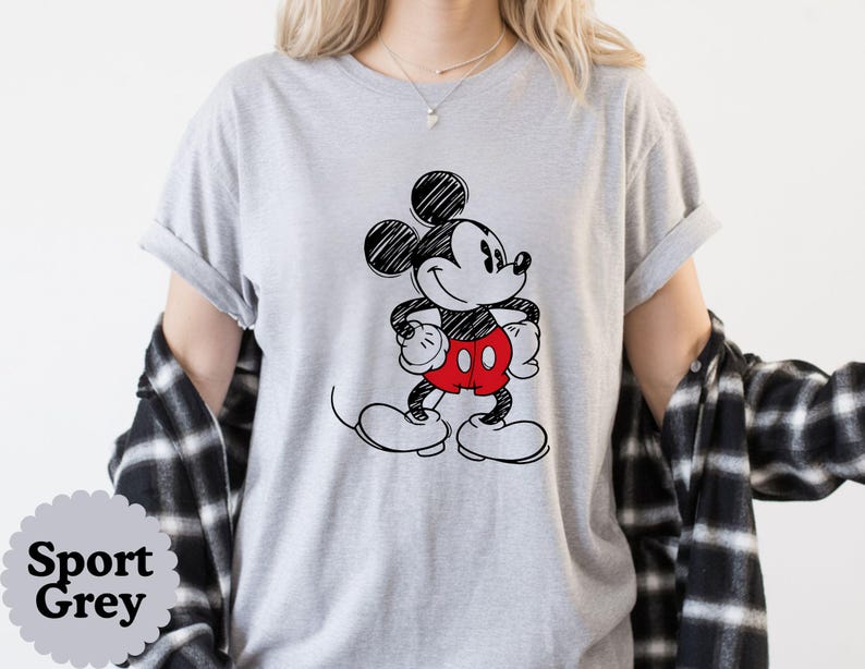 May include: Sport Grey t-shirt featuring a black and white sketch of Mickey Mouse with red shorts and white gloves and shoes. The shirt has rolled-up sleeves. The words "Sport Grey" are in a gray circle at the bottom left.