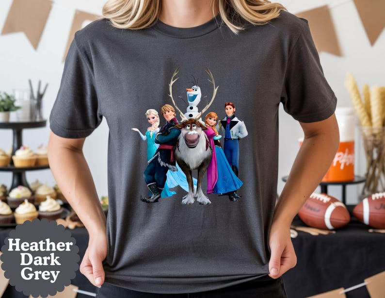 May include: A heather dark grey short-sleeved t-shirt featuring a graphic print of the characters Elsa, Kristoff, Olaf, Sven, Anna, and Hans from the movie Frozen. The design is centred on the chest of the shirt, displaying the characters together.