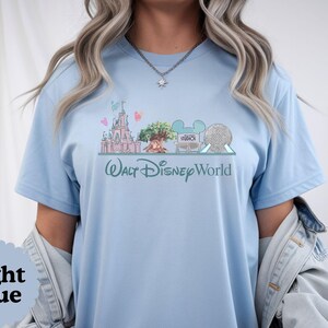 May include: Light blue t-shirt with a Walt Disney World design. The graphic shows a castle, the Tree of Life, and Spaceship Earth. The words "Walt Disney World" are written in a script font.