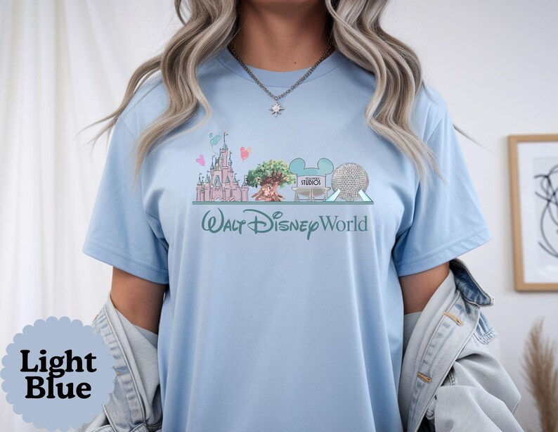 May include: Light blue t-shirt with a Walt Disney World design. The graphic shows a castle, the Tree of Life, and Spaceship Earth. The words "Walt Disney World" are written in a script font.