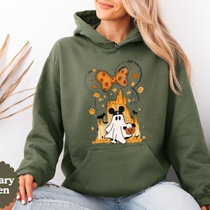 May include: A military green hooded sweatshirt featuring a graphic print of a white ghost wearing black mouse ears, holding a small orange pumpkin bucket, standing in front of a castle silhouette with orange pumpkins, bats, and a bow.