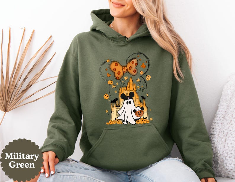 May include: A military green hooded sweatshirt featuring a graphic print of a white ghost wearing black mouse ears, holding a small orange pumpkin bucket, standing in front of a castle silhouette with orange pumpkins, bats, and a bow.