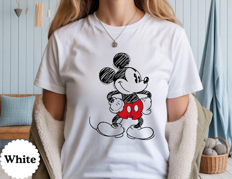 May include: White t-shirt featuring a black and red Mickey Mouse graphic. The cartoon character is drawn in a sketch style, with his signature red shorts and white gloves. The word "White" is printed on a white circle.