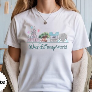 May include: White t-shirt with a colourful illustration of Walt Disney World landmarks, including a castle, tree, and Spaceship Earth. The words "Walt Disney World" are written in a teal script below the images.
