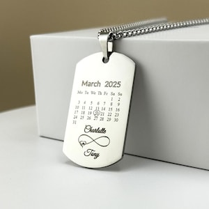 Puede incluir: Collar de plata con un colgante de placa de identificación con un calendario para marzo de 2025 con la fecha 20 en círculo. El colgante también tiene el texto "Charlotte" y "Tony" grabado.