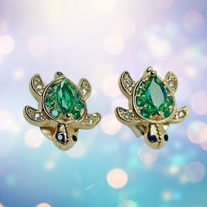 Könnte beinhalten: Ein Paar goldfarbene Schildkröten-Ohrstecker mit grünen und klaren Kristall-Akzenten.