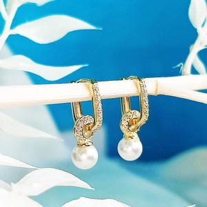 May include: A pair of gold hoop earrings with a pearl drop and a row of clear cubic zirconia stones.