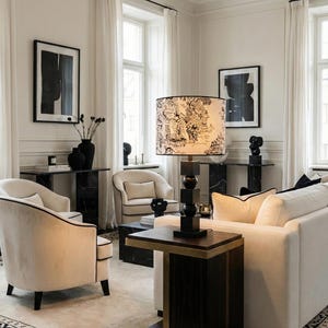 May include: A stylish living room featuring cream-coloured furniture, including a sofa and armchairs, with black detailing. A patterned lampshade sits on a dark wooden lamp base. Black and white artwork and vases complete the sophisticated decor.