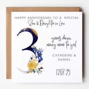 Może przedstawiać: Biała kartka rocznicowa z brązową kopertą. Karta zawiera tekst "HAPPY ANNIVERSARY TO A SPECIAL Son & Daughter in Law" i "years down, many more to go!". Granatowa liczba 3 jest ozdobiona złotem i kwiatami.