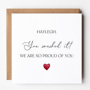 Può includere: Biglietto di auguri bianco con busta marrone. Il biglietto presenta il testo "HAYLEIGH, You smashed it! WE ARE SO PROUD OF YOU" in nero. Un cuore rosso in basso.