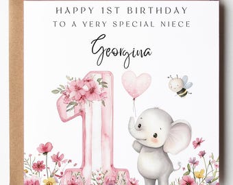 May include: A square greeting card featuring the text HAPPY 1ST BIRTHDAY TO A VERY SPECIAL NIECE and the name Georgina. The design includes a large pink number one decorated with flowers, a small gray elephant holding a pink heart balloon, and a bee.