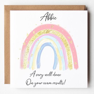 Può includere: Biglietto di auguri bianco con un arcobaleno pastello e dettagli glitterati dorati. Il biglietto riporta il nome "Abbie" e il messaggio "A very well done On your exam results!". Presentato con una busta marrone.