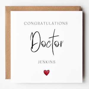 Op de afbeelding: Een witte wenskaart met de woorden "CONGRATULATIONS Doctor JENKINS" in zwart schrift. Onderaan staat een klein rood hart. De kaart zit in een bruine envelop.