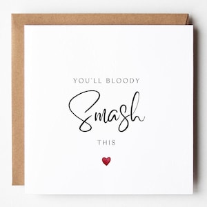 Può includere: Biglietto di auguri bianco con la scritta "YOU'LL BLOODY Smash THIS" in corsivo nero. Un piccolo cuore rosso in basso. Il biglietto è in una busta marrone.