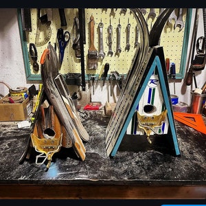 May include: Two wooden birdhouses made from repurposed skis. The birdhouses are painted in blue, white, and red. One birdhouse has a small, gold metal bird perched on the front.