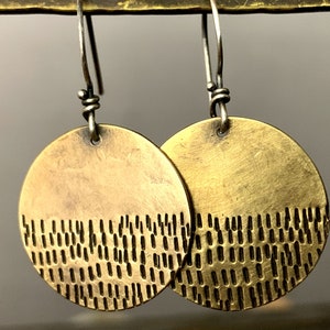 May include: A pair of brass earrings with a textured pattern on the bottom half of each earring. The earrings are hanging from silver hooks.