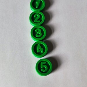 May include: Five green plastic circles with white numbers 1 through 5 on a white background.