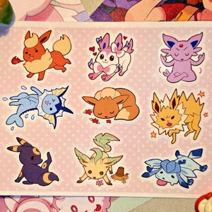 Puede incluir: Una hoja de pegatinas con criaturas de dibujos animados en varias poses y colores. Las pegatinas incluyen personajes como Eevee, Vaporeon y Jolteon, con un fondo rosa y el texto "eeveelutions" en el lateral.