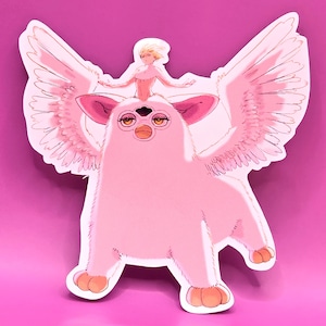 Puede incluir: Una pegatina rosa que representa una criatura parecida a un Furby con grandes alas y una pequeña figura montada en su cabeza. La criatura tiene orejas grandes, tres ojos y pies naranjas. Las alas y la figura están delineadas en dorado.