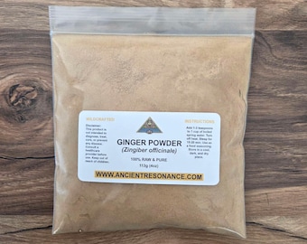 Op de afbeelding: Een doorzichtige plastic zak gevuld met lichtbruin gemberpoeder. Een wit etiket toont de tekst "GINGER POWDER (Zingiber officinale) 100% RAW & PURE 113g (4oz)" en instructies. De zak is verzegeld en ligt op een houten oppervlak.