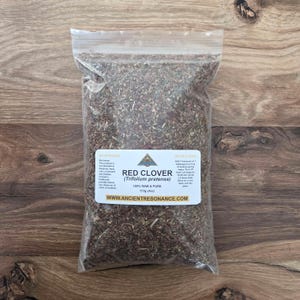 Puede incluir: Una bolsa transparente llena de trébol rojo seco (Trifolium pratense). La bolsa tiene una etiqueta blanca con el texto "Red Clover" y "100% Raw & Pure". La bolsa contiene 113 gramos de producto.