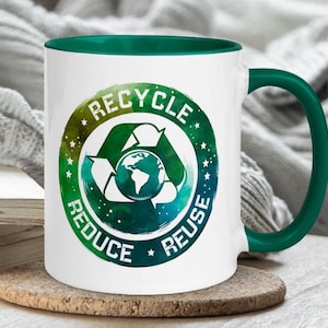 Puede incluir: Taza de cerámica blanca con borde y asa verdes. La taza presenta un diseño de acuarela verde, azul y blanco de un símbolo de reciclaje con las palabras "Reciclar, Reducir, Reutilizar" alrededor.
