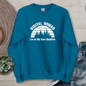 Może przedstawiać: Niebieska bluza w kolorze indygo z napisem "DIGITAL NOMAD" nad grafiką lasu i napisem "I'm on My Own Deadline". Bluza ma okrągły dekolt.