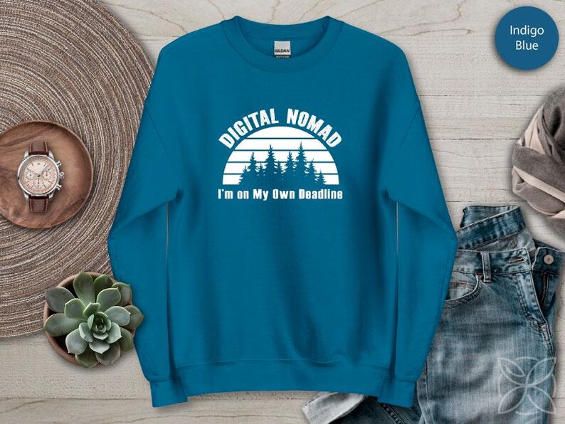 Może przedstawiać: Niebieska bluza w kolorze indygo z napisem "DIGITAL NOMAD" nad grafiką lasu i napisem "I'm on My Own Deadline". Bluza ma okrągły dekolt.